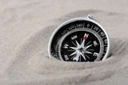 a compass part buried in sand with needle pointing north